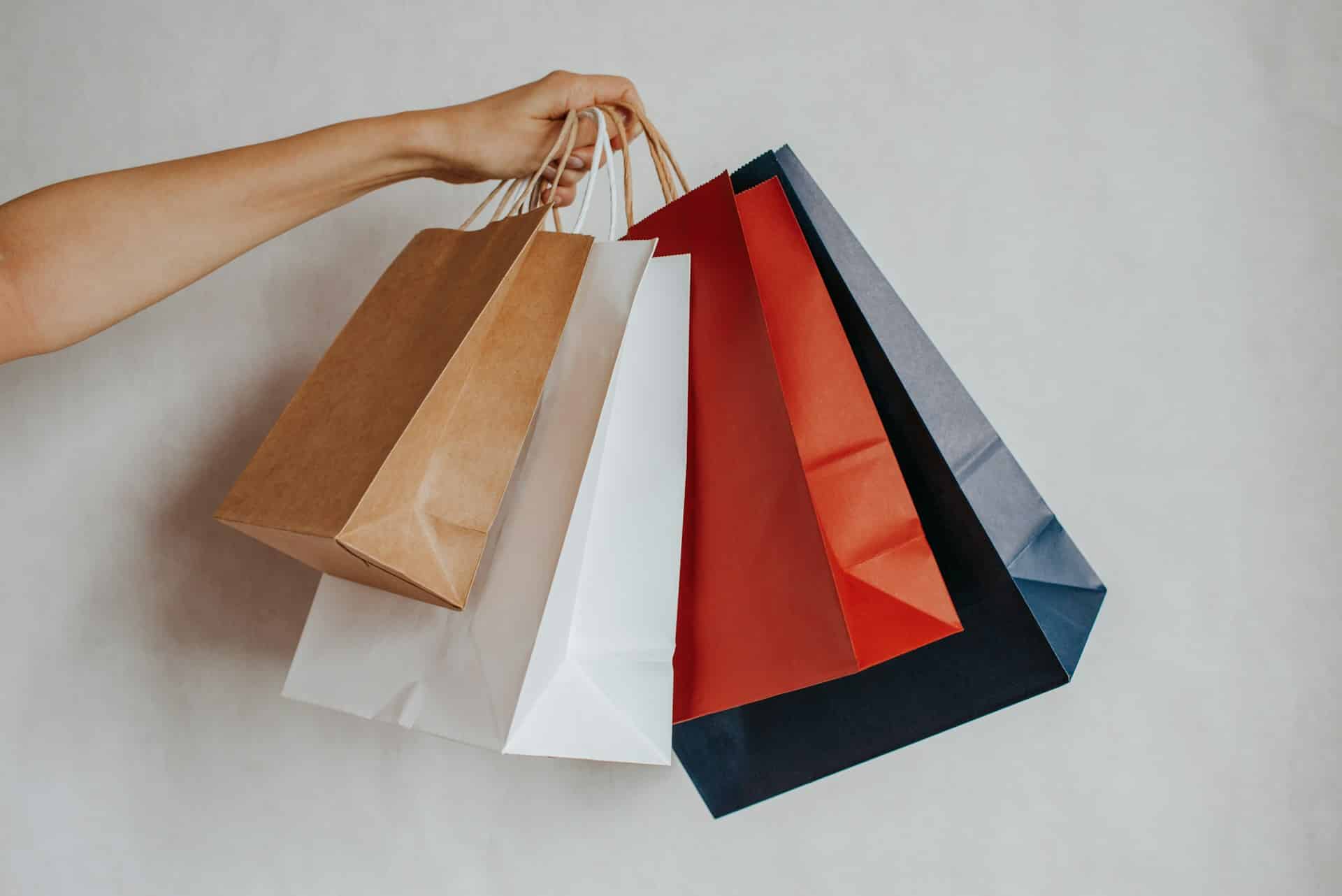 Hand holding colorful shopping bags against a light background